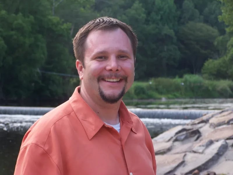 John Tobey smiling outdoors near a waterfall